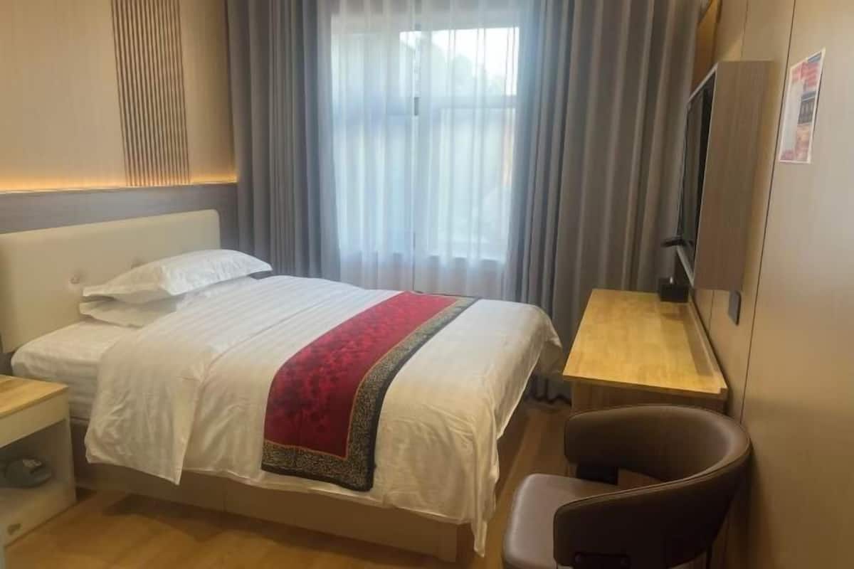 A hotel room with a bed, a desk, a chair, a TV, and a window with curtains.