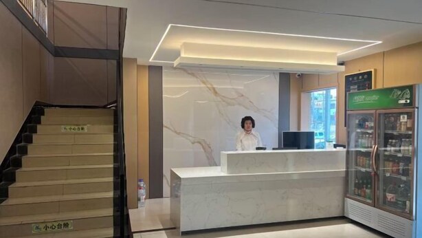 A hotel reception area with a marble counter, a staircase, and a refrigerated display case. - Daguang Hotel (Turpan)