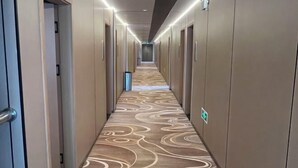 A hotel hallway with a patterned carpet, doors, and a trash bin. - Daguang Hotel (Turpan)