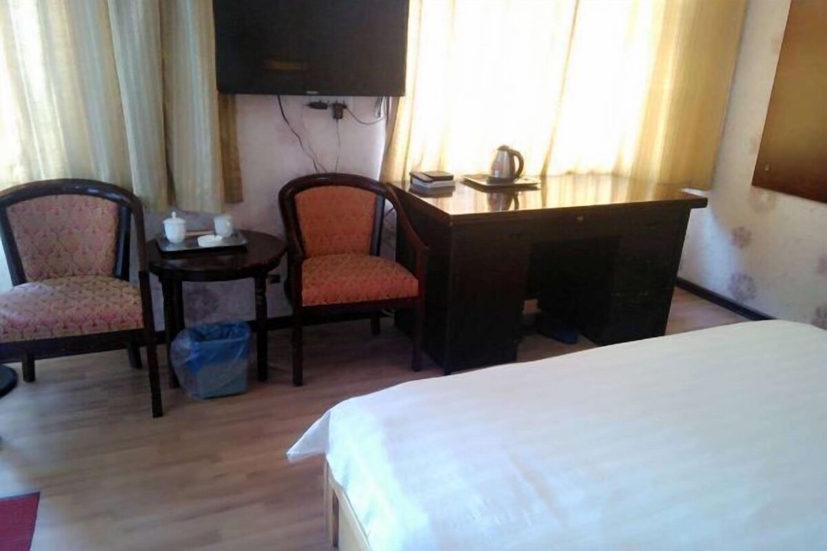 Una habitación de hotel con cama, dos sillas, escritorio, televisor y ventana con cortinas.