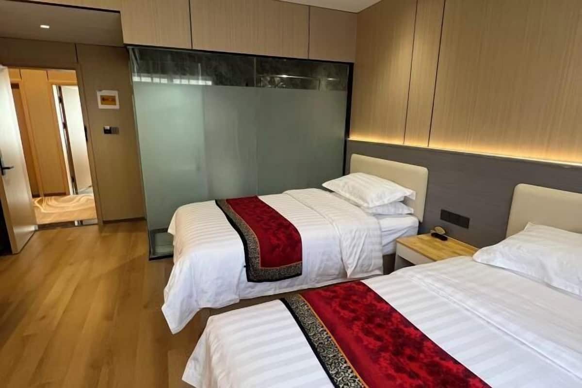 A hotel room with two beds, a wooden floor, and a glass partition wall.