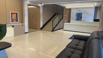 A hotel lobby with a reception desk, a staircase, a sofa, and a plant.