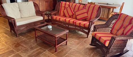 A living room with wicker furniture, a coffee table, and a kitchen in the background.