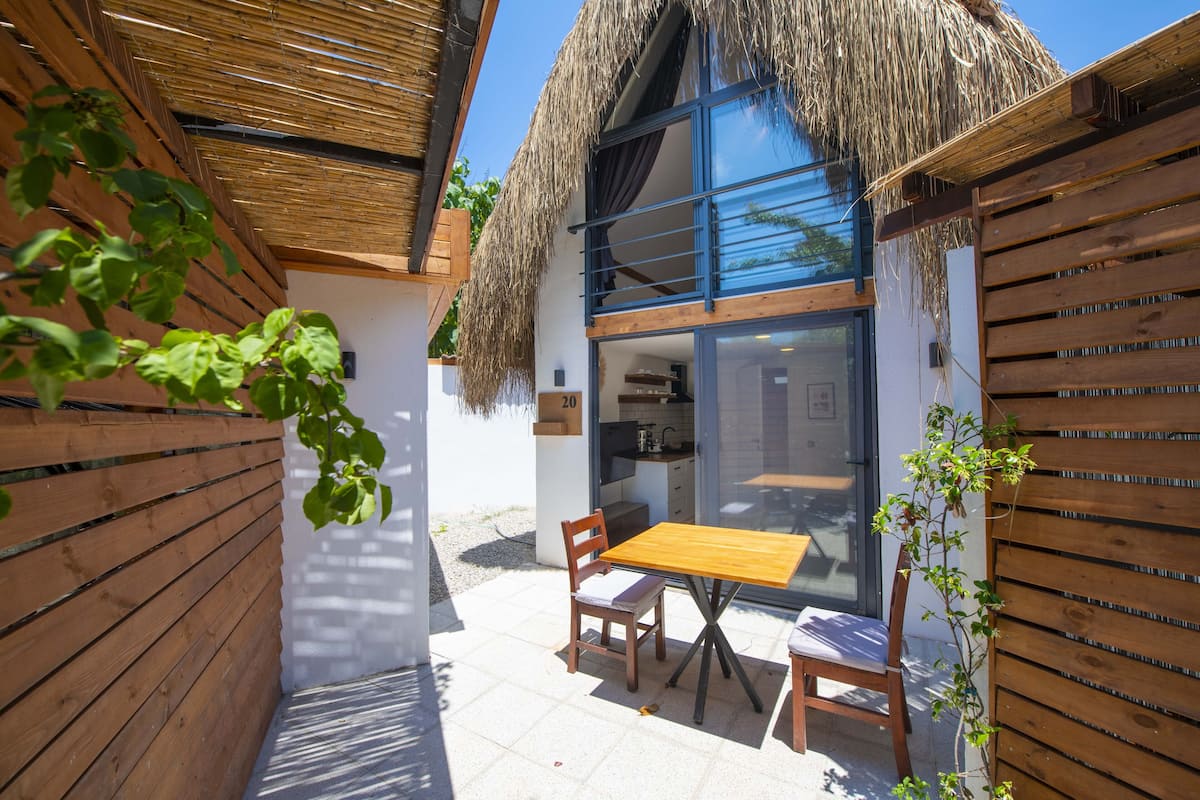 A small, modern house with a thatched roof, a wooden table, and two chairs outside.