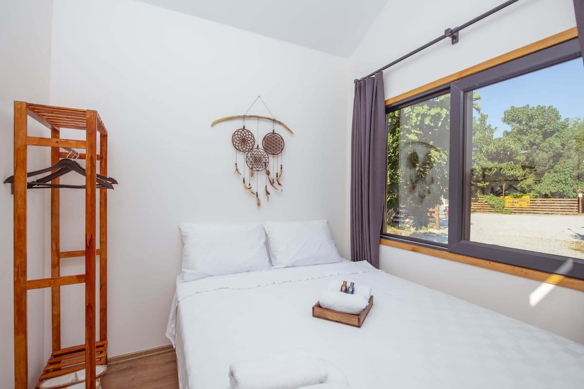 A neatly made bed with white linens, a wooden hanger rack, and a dreamcatcher decoration on the wall.