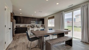 A modern kitchen with dark cabinets, a large wooden table, and a sliding glass door leading to a patio.