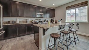 A modern kitchen with dark cabinets, a central island, bar stools, and a large window.