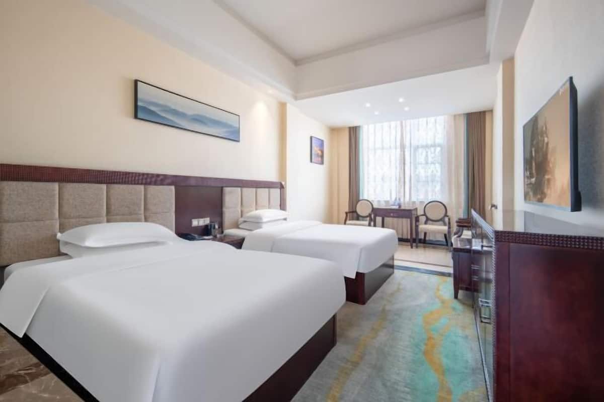 A hotel room with two beds, a desk, and a chair.