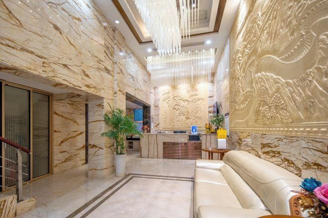 A hotel lobby with marble walls, a reception desk, a sofa, and a chandelier.