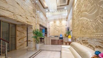 A hotel lobby with marble walls, a reception desk, a sofa, and a chandelier.