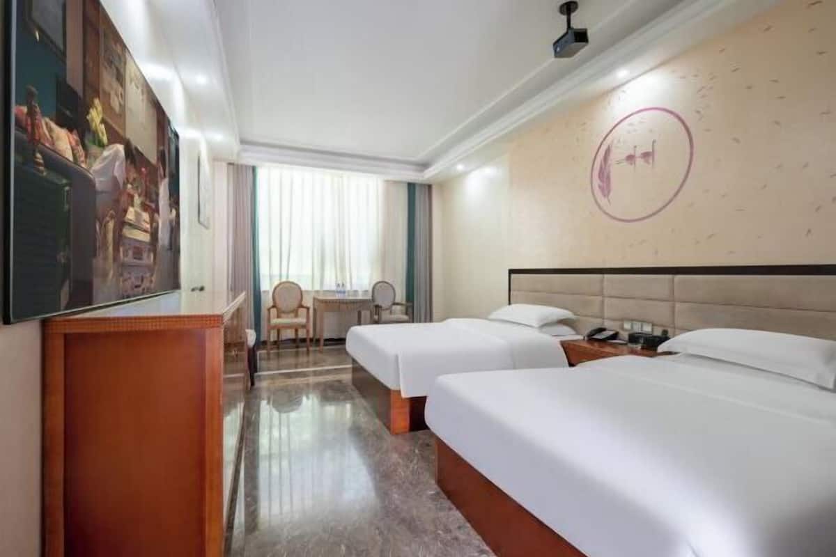 A hotel room with two beds, a desk, a chair, and a large wall-mounted TV.