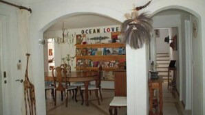Ein Essbereich mit Holztisch und Stühlen, einem Bücherregal mit der Aufschrift 'OCEAN LOVE' und einem dekorativen Federobjekt.