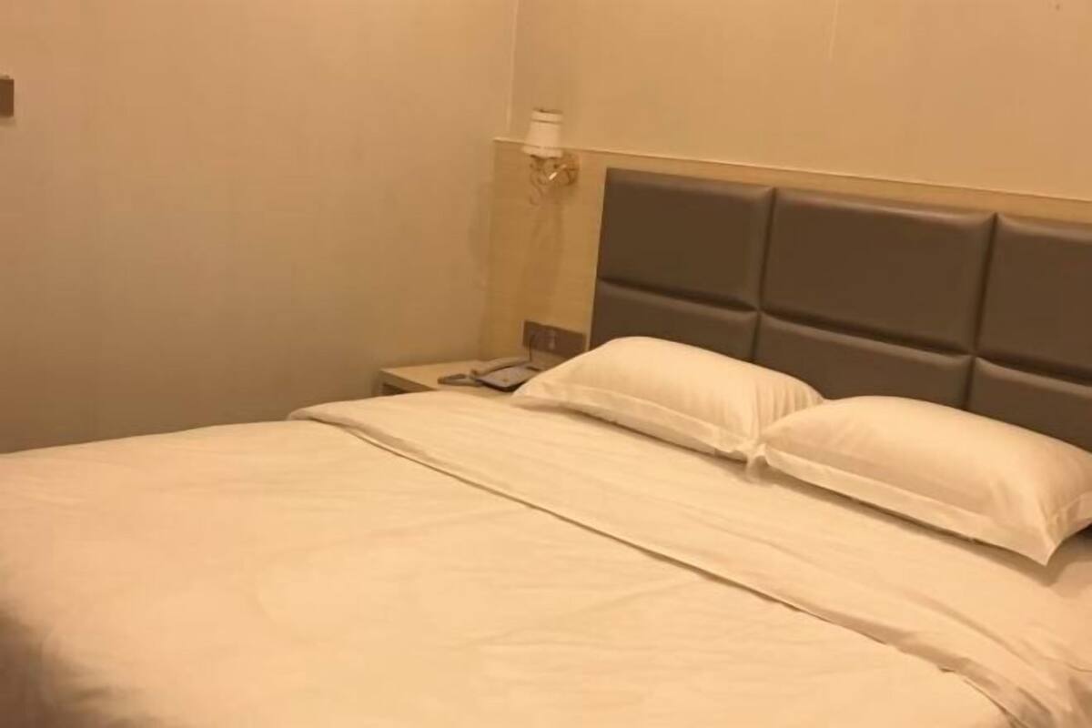 A hotel room with a bed, a nightstand, and a wall-mounted lamp.