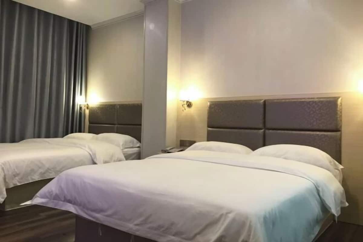 A hotel room with two beds, a large window with curtains, and a wall-mounted light fixture.