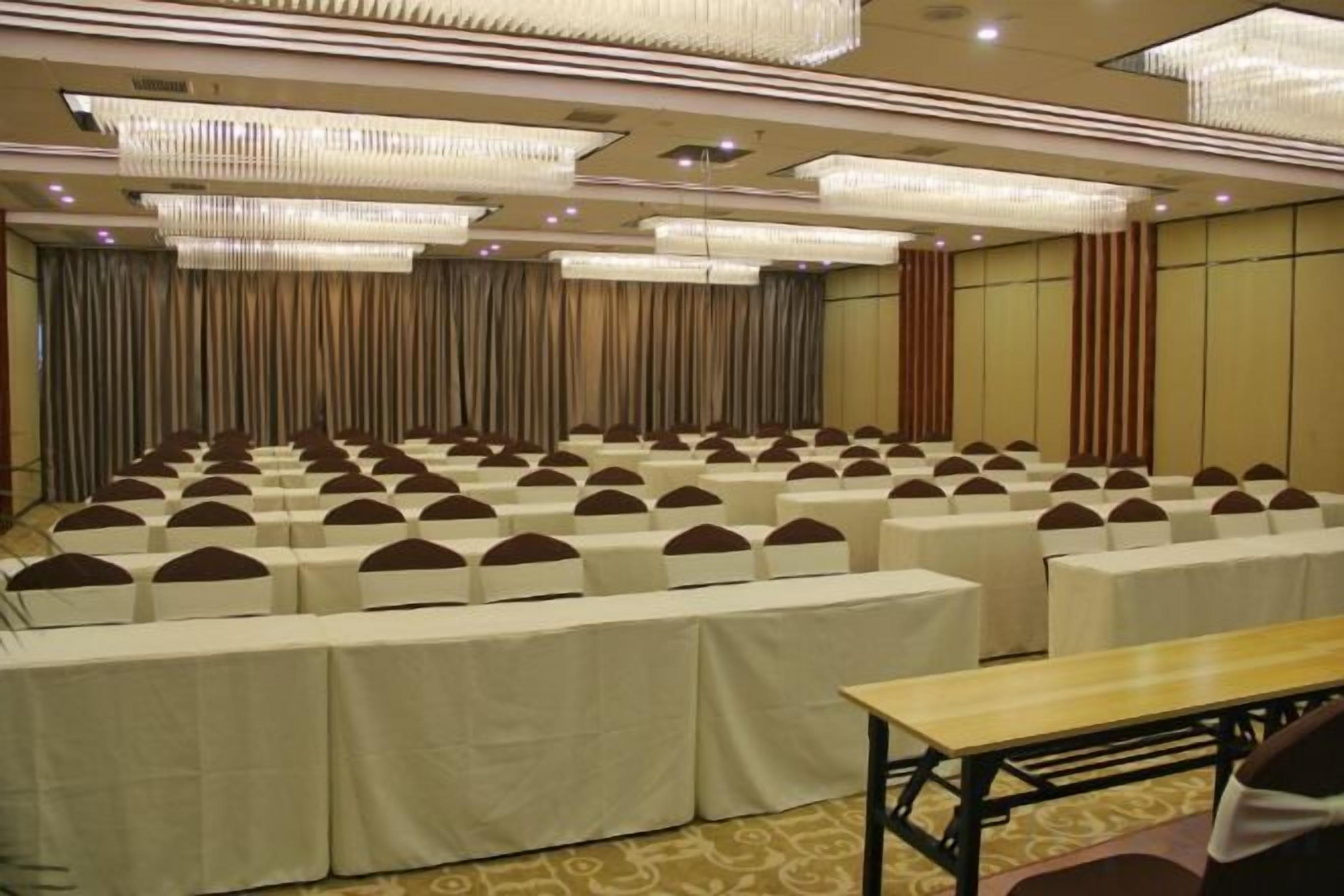 A conference room with rows of tables and chairs, large chandeliers, and a curtain backdrop.