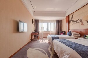 Habitación de hotel con dos camas, un escritorio, una silla, un televisor y un ventanal con cortinas.