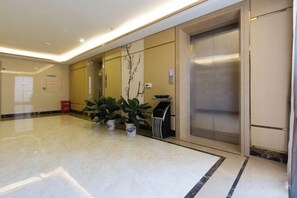 A hotel lobby with a marble floor, potted plants, an elevator, and a trash bin.