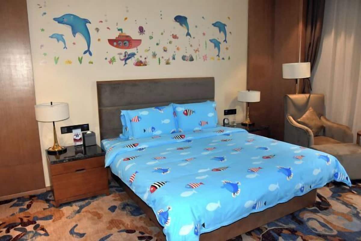 Habitación de hotel con cama, mesitas de noche, una silla y un muro decorado con motivos marinos.
