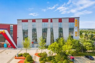 Un edificio moderno con fachada roja y blanca, una escalera roja y un estacionamiento con árboles.