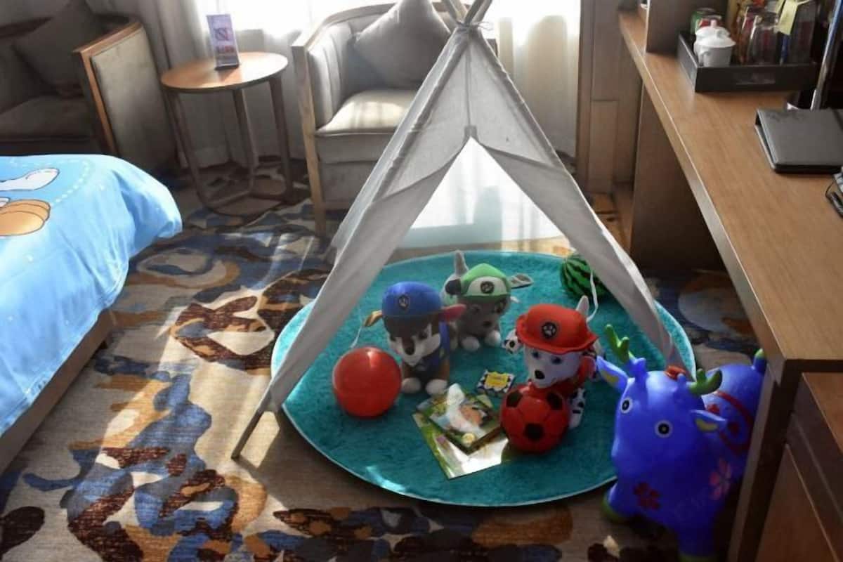 Una habitación de hotel con cama, una mesa redonda, una silla, una tienda de campaña pequeña y juguetes en el suelo.
