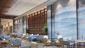 Eine geräumige Lobby mit Marmorboden, Sitzbereichen mit Sofas und Sesseln, einem großen Bücherregal und einem Wandgemälde einer Landschaft.