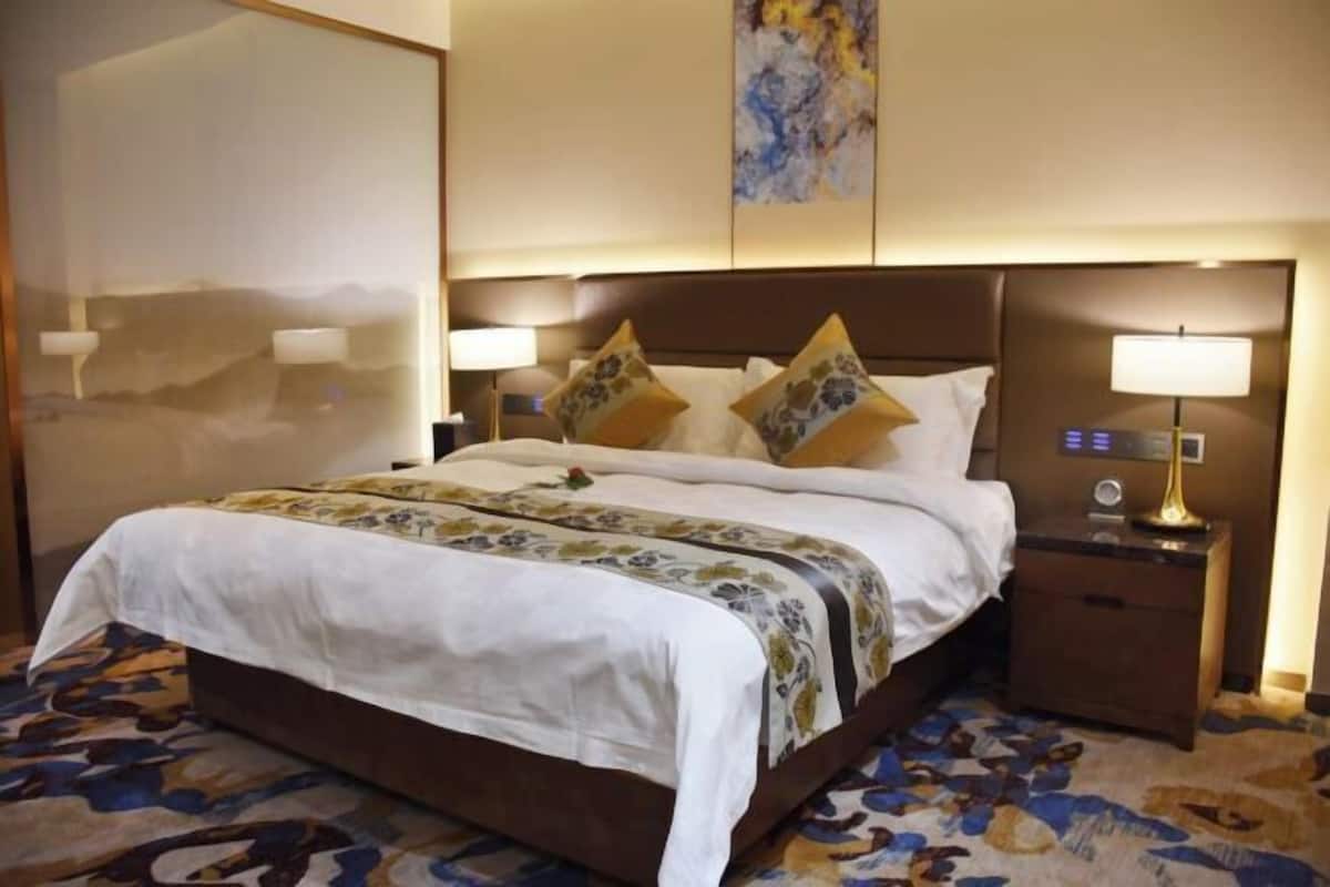 Habitación de hotel con una cama grande, dos mesitas de noche con lámparas, un cuadro en la pared y una alfombra estampada.