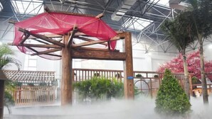 Eine Holzkonstruktion mit rotem Baldachin, umgeben von Nebel, in einem Gebäude mit hoher Decke und Metallgerüst.