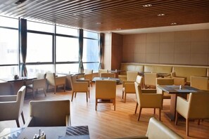 Un lobby moderno de hotel con varias zonas de estar, ventanas amplias y un techo alto.