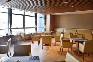 Un lobby moderno de hotel con varias zonas de estar, ventanas amplias y un techo alto.