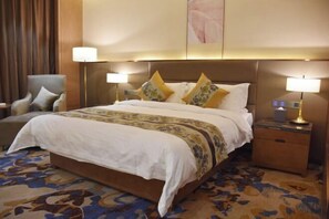 Una habitación de hotel con una cama grande, dos lámparas de noche, una silla y una mesita de noche.