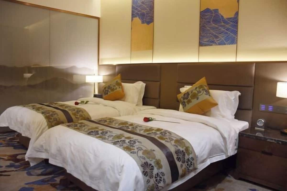 Habitación de hotel con dos camas, un espejo grande, obras de arte en la pared y una mesita de noche con lámpara.