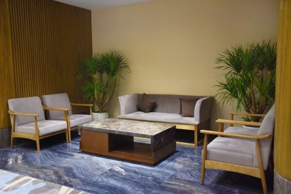A modern lounge area with a sofa, two armchairs, and a coffee table. There are potted plants and a wooden panel wall. - Luxinan Hot Spring Hotel (Heze)