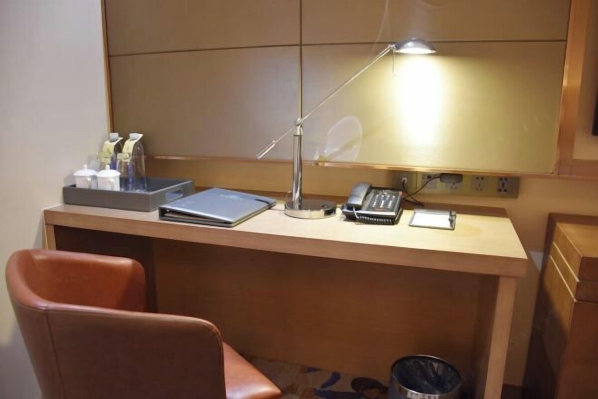 A hotel room desk with a laptop, a telephone, a lamp, and a trash bin.