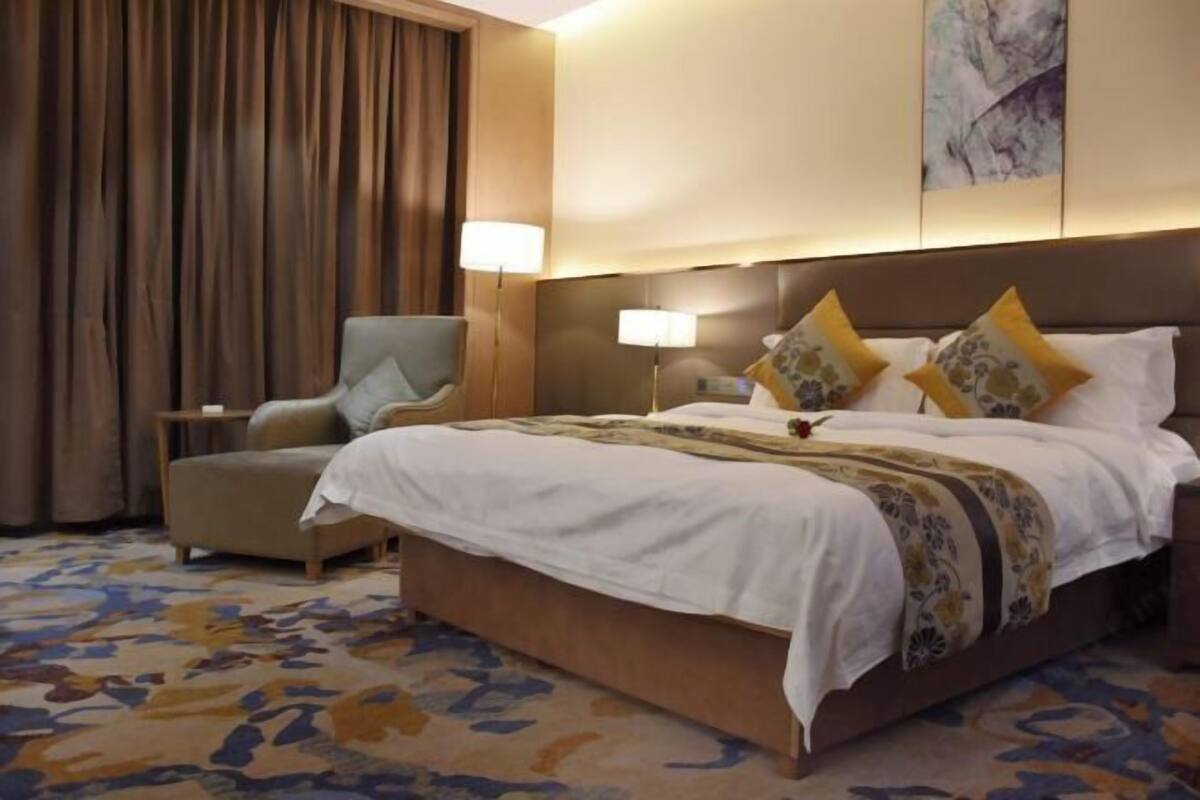 Una habitación de hotel con una cama grande, una silla, una mesita de noche y una lámpara.