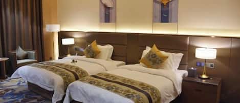 A hotel room with two beds, a large window with curtains, a bedside table with a lamp, and a wall-mounted clock.