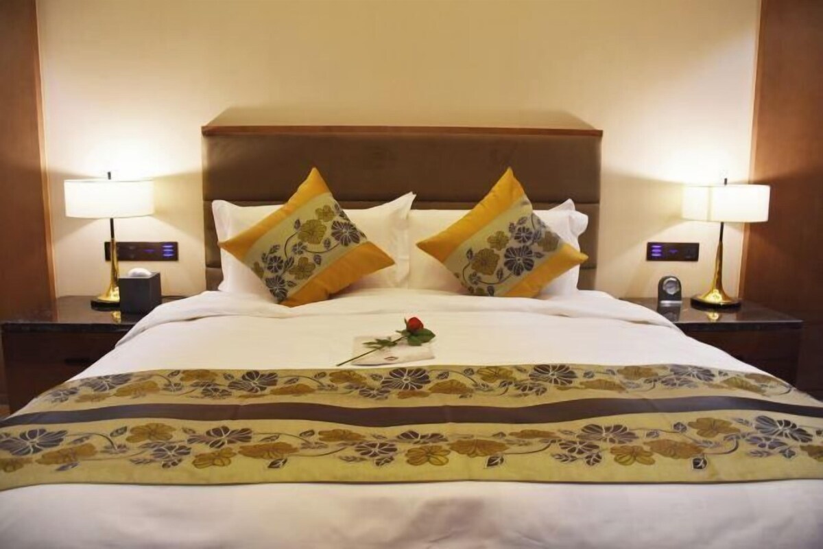 A hotel room with a bed, two nightstands, a digital clock, and a floral bedspread.