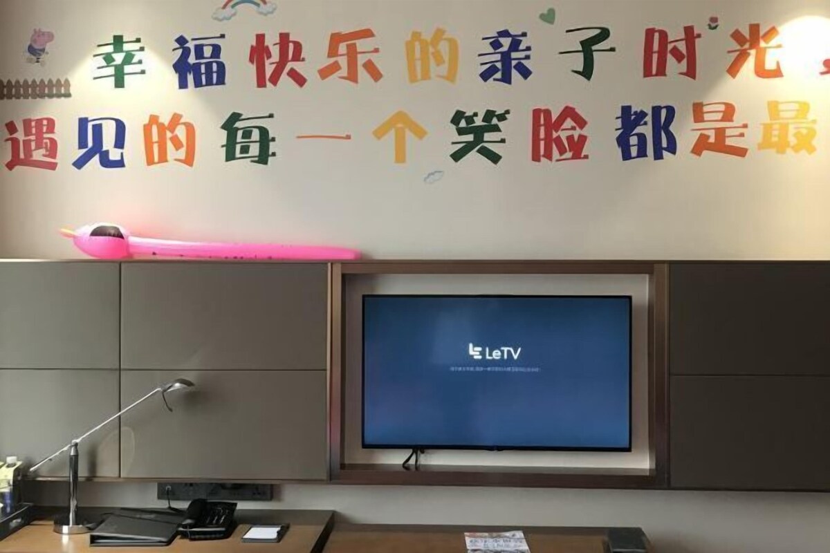 A room with a television displaying 'LeTV', a desk with a lamp, and a wall with colorful text.