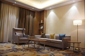 A well-lit living room with a sofa, armchair, and coffee table, featuring a patterned carpet and a lamp. - Luxinan Hot Spring Hotel (Heze)