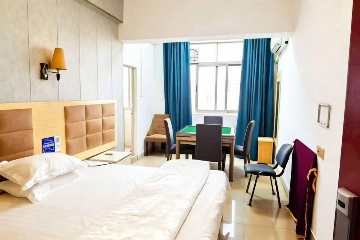 Une chambre d’hôtel avec un lit, un bureau et une chaise, une lampe et une fenêtre avec des rideaux.