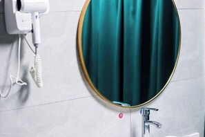 A bathroom with a round mirror, a white hairdryer, and a sink. - Jinhongye Hotel (Dongguan)