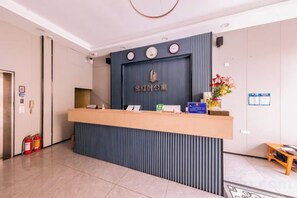 Un comptoir d’accueil avec une horloge, un extincteur et une petite table ornée de fleurs.