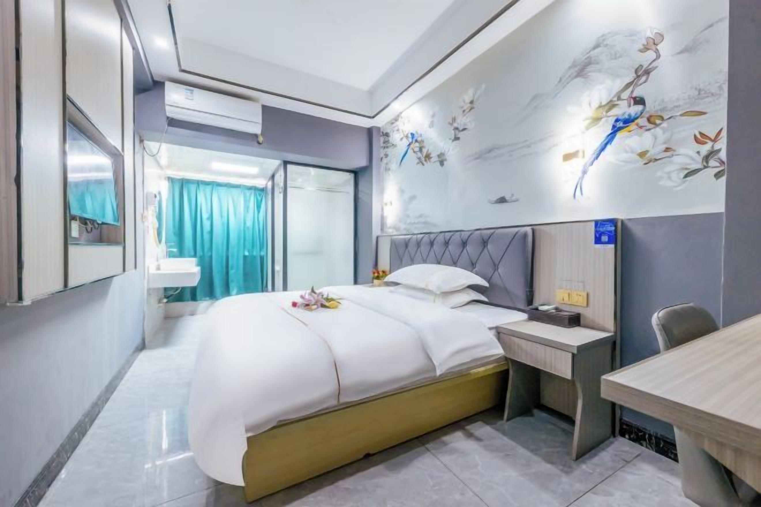 Camera d'albergo moderna con un letto grande, una scrivania e una sedia. Si vede una finestra con tende, un condizionatore d'aria a parete e un murale decorativo.