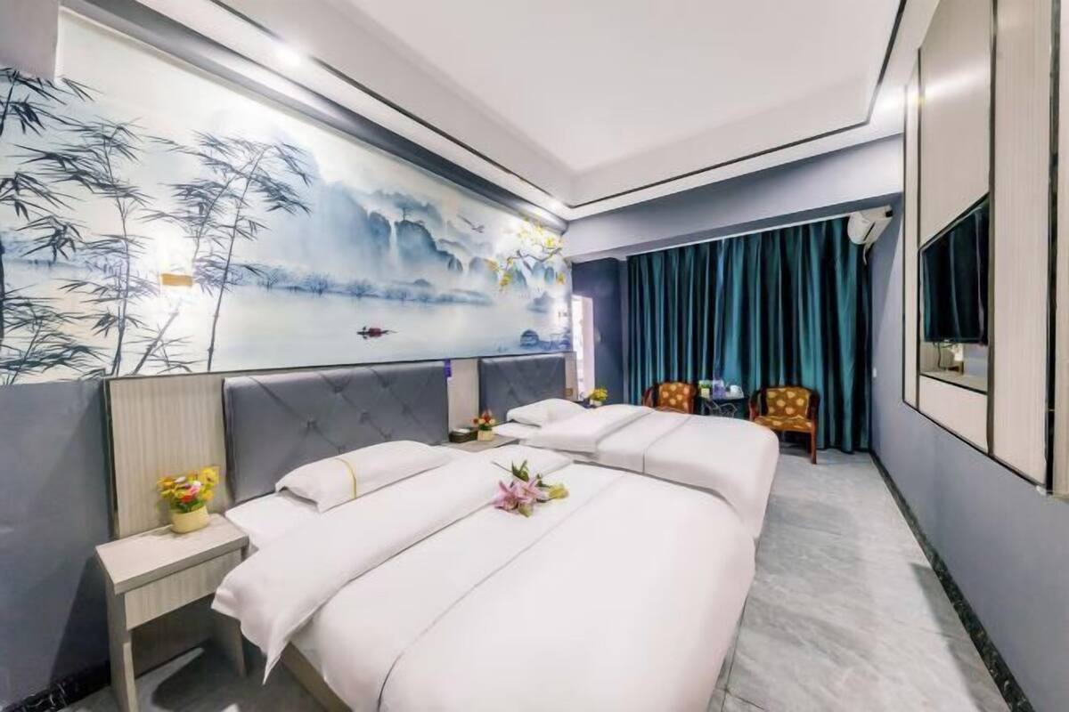 Une chambre d’hôtel avec deux lits, une grande fresque murale, une télévision et un fauteuil.