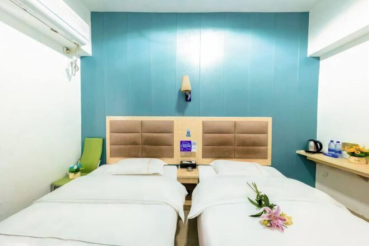 Une chambre d’hôtel avec deux lits, une tête de lit en bois, une table de chevet, une lampe et une petite étagère avec des articles de toilette.