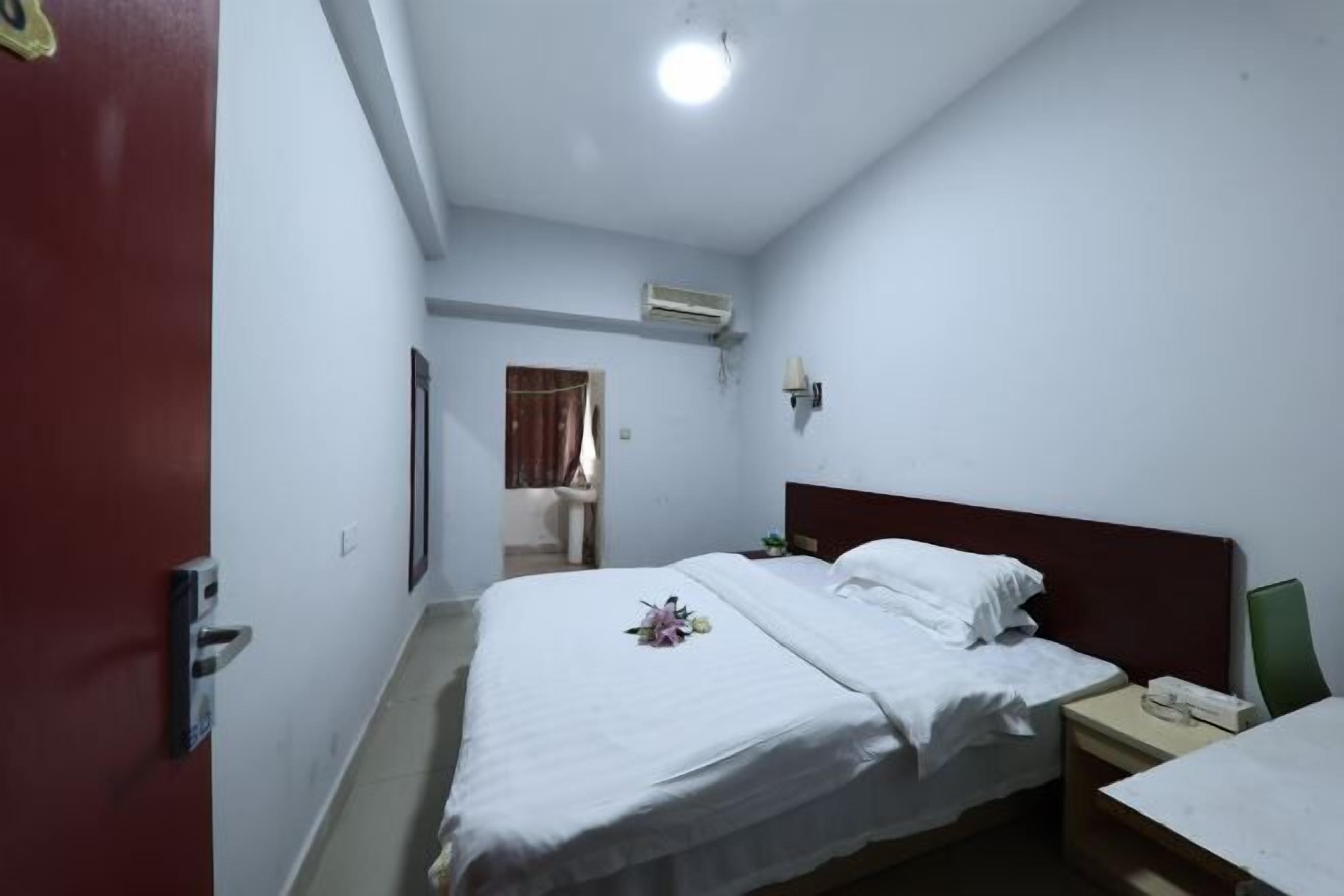 A hotel room with a bed, bedside table, and an air conditioning unit.