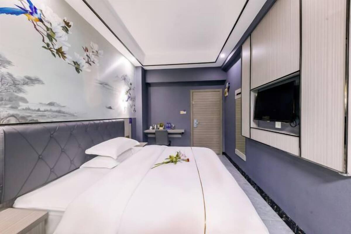 Une chambre d’hôtel équipée d’un lit, d’un bureau, d’une télévision et d’un mur orné d’une fresque florale.