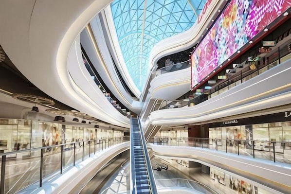 A multi-level shopping mall with escalators, glass railings, and a central skylight.