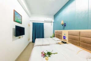Habitación de hotel con dos camas, un televisor de pantalla plana, un equipo de aire acondicionado, una cortina azul y una lámpara fijada a la pared.