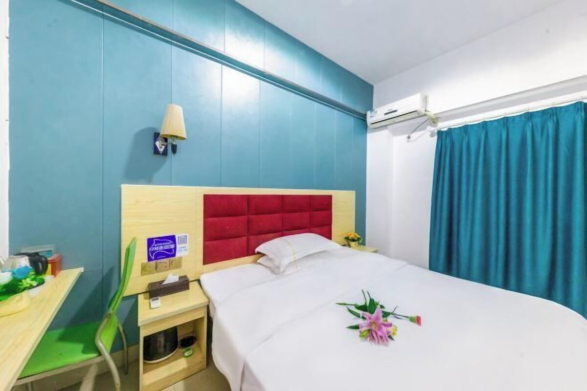 Habitación de hotel con cama, escritorio, silla, mesita de noche, lámpara y ventana con cortinas.