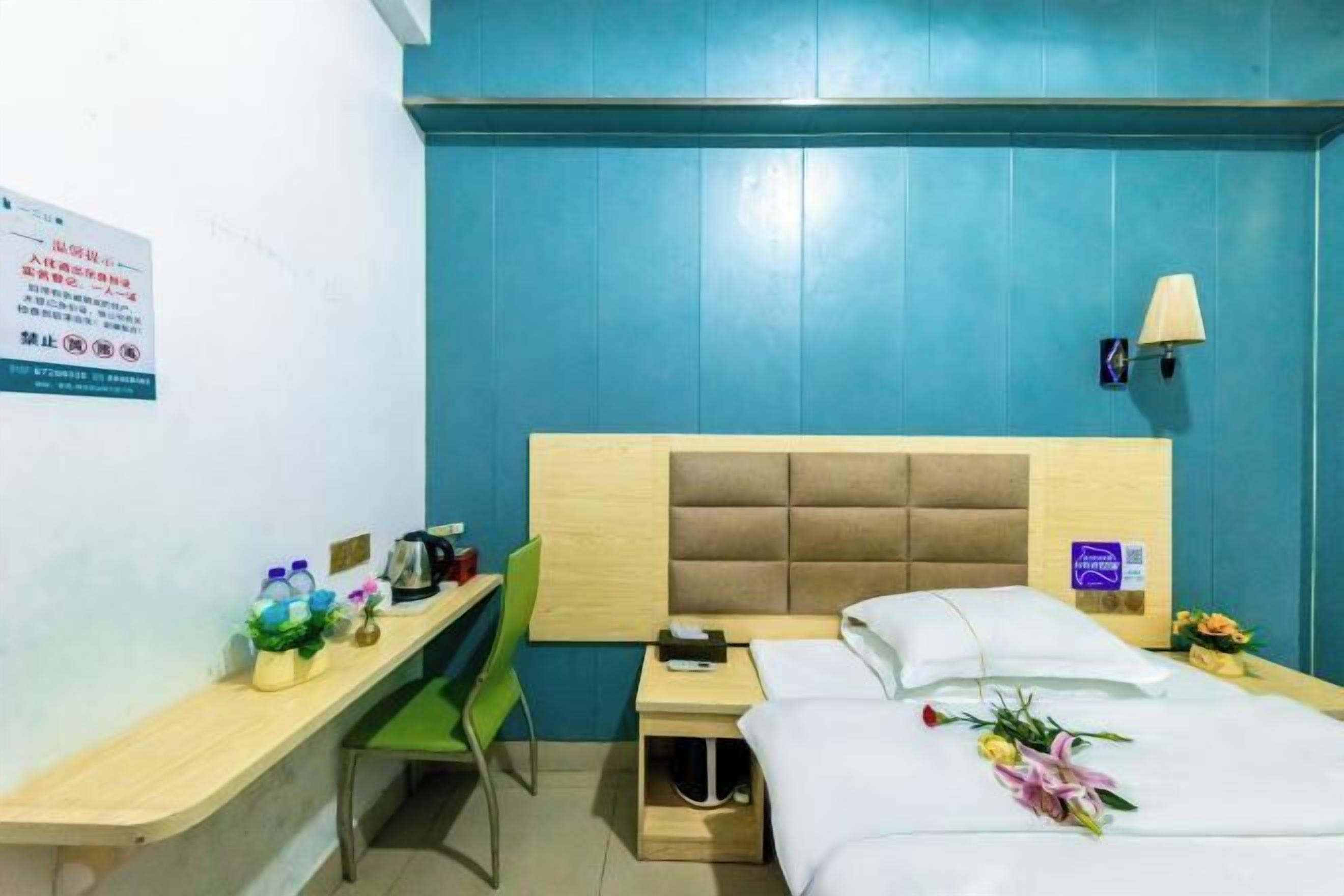 Une chambre d’hôtel avec une tête de lit en bois, un bureau avec une chaise, un lit avec une literie blanche et une table de chevet avec une lampe.